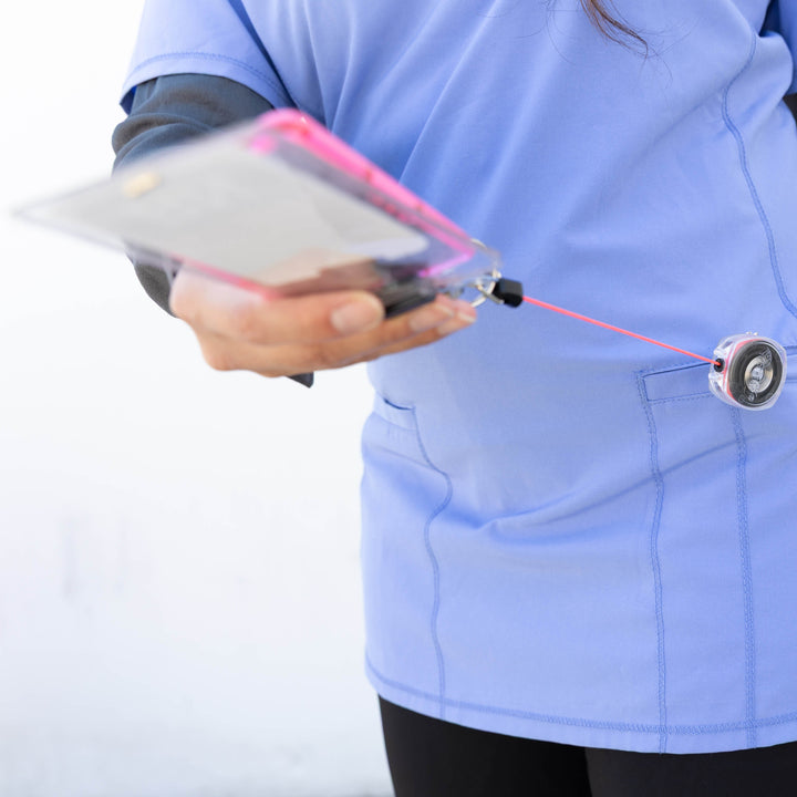 Person wearing a blue scrub top holding a badge reel with pink cord and swivel clip against a white background